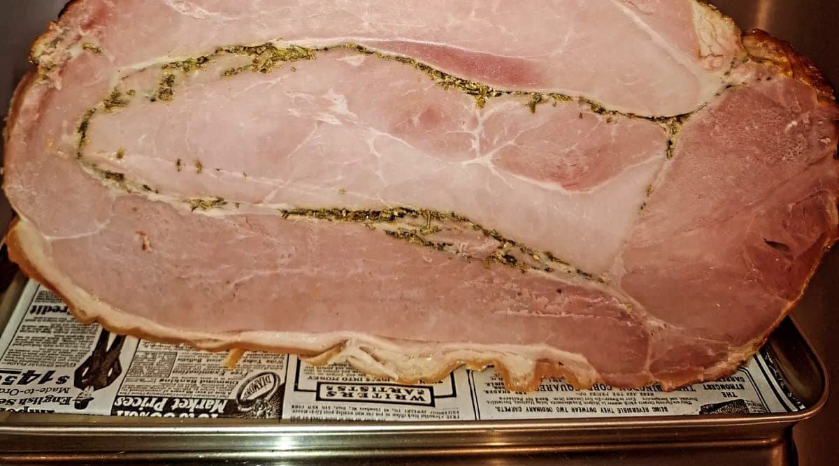 Un jambon cuit entier aux herbes sur son plateau, au comptoir, avant d’être tranché